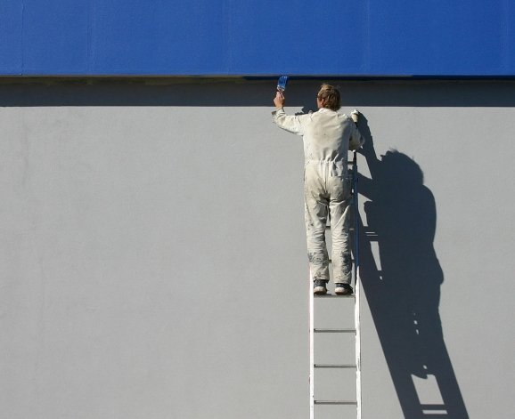 Homem fazendo pintura comercial em fachada.